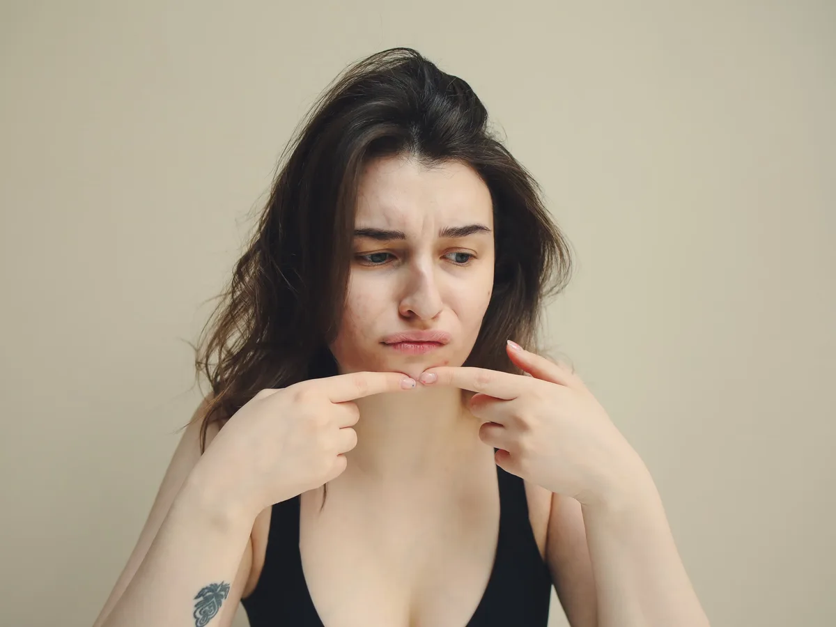 Close-up of a woman touching a spot on her chin, examining her skin in the light.