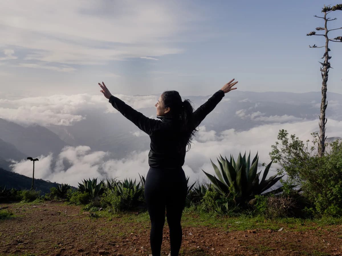Una mujer de pie en la cima de una montaña con los brazos abiertos.
