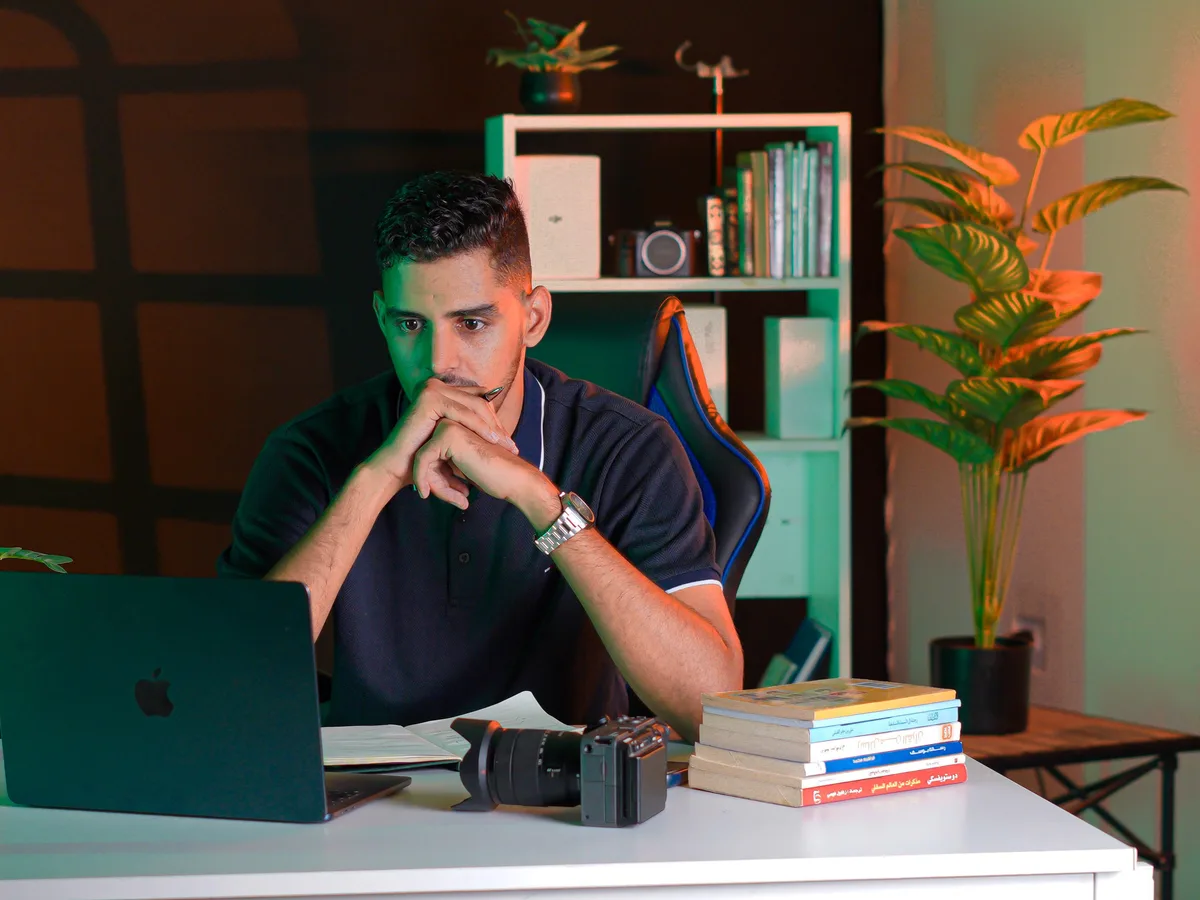 Un hombre concentrado trabajando en un escritorio ordenado con un portátil y libros.