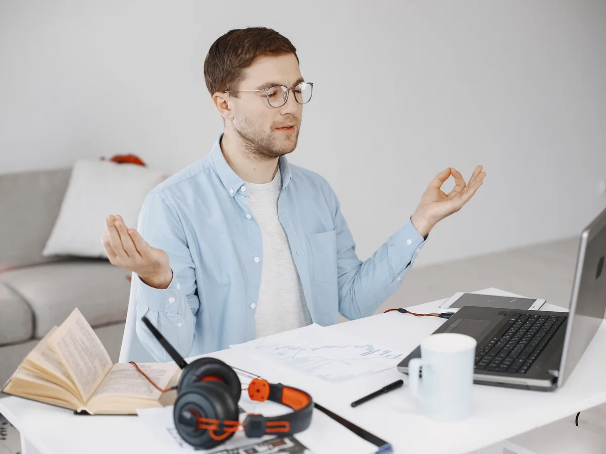 A man sitting calmly at his desk with his eyes closed, taking a slow breathing break away from his work.