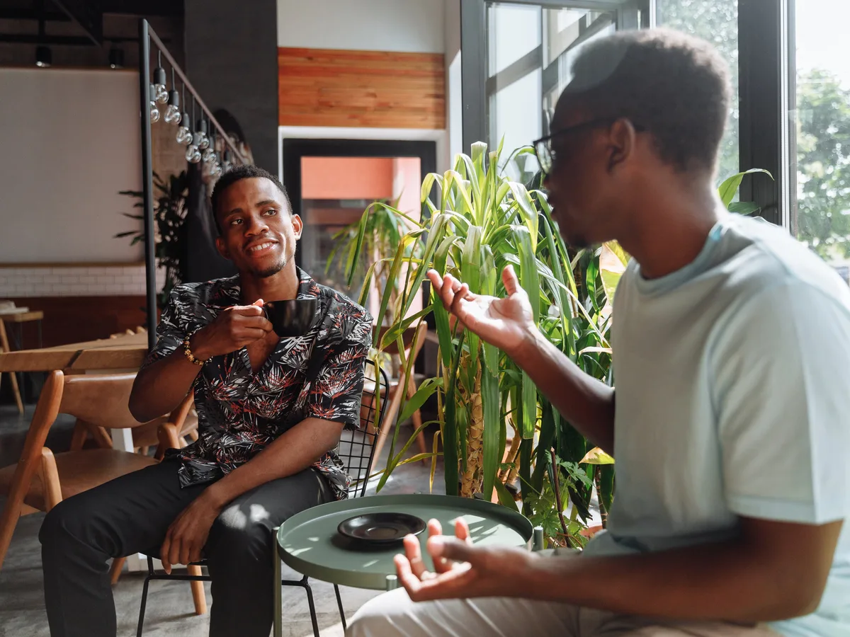 Dos hombres tomando café y conversando junto a una ventana.