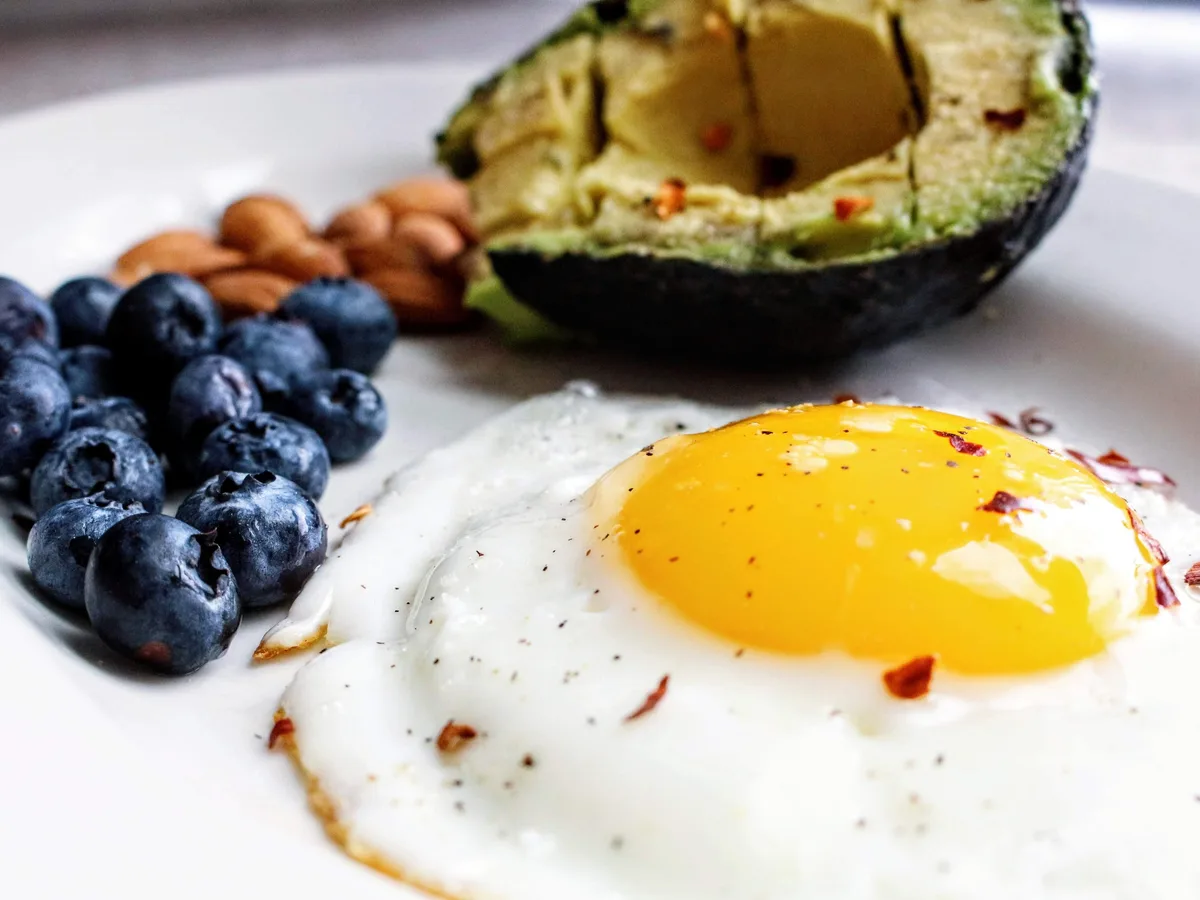 Huevera abierta con huevos morenos junto a arándanos, alimentos sencillos que cubren la proteína