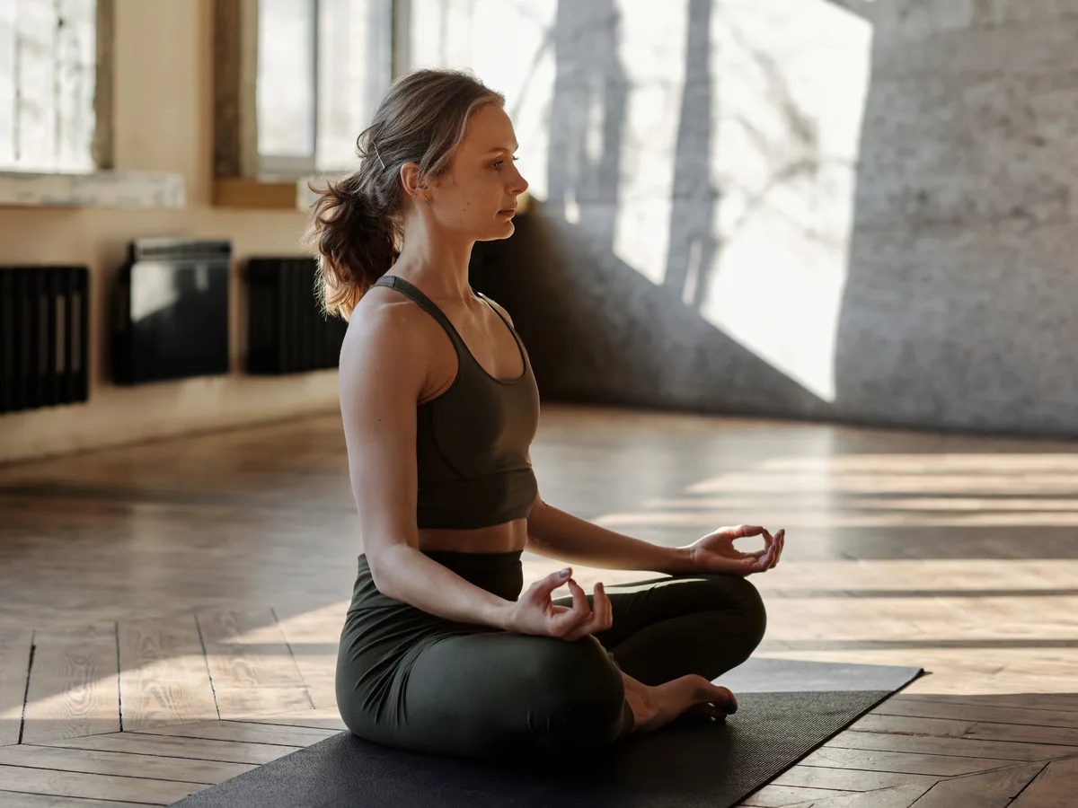 Una mujer sentada tranquilamente en postura de yoga, entrenando una mente serena y concentrada.