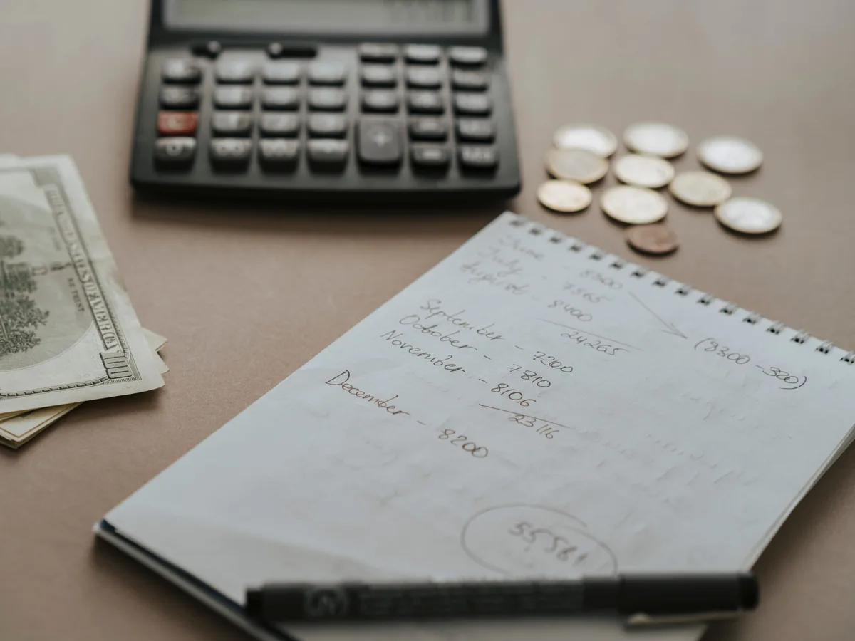 Un escritorio con una calculadora, billetes, monedas y notas para planificar un presupuesto mensual