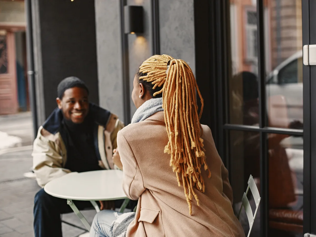 Un hombre y una mujer sentados en la terraza de una cafetería, charlando y sonriendo en una conversación relajada.