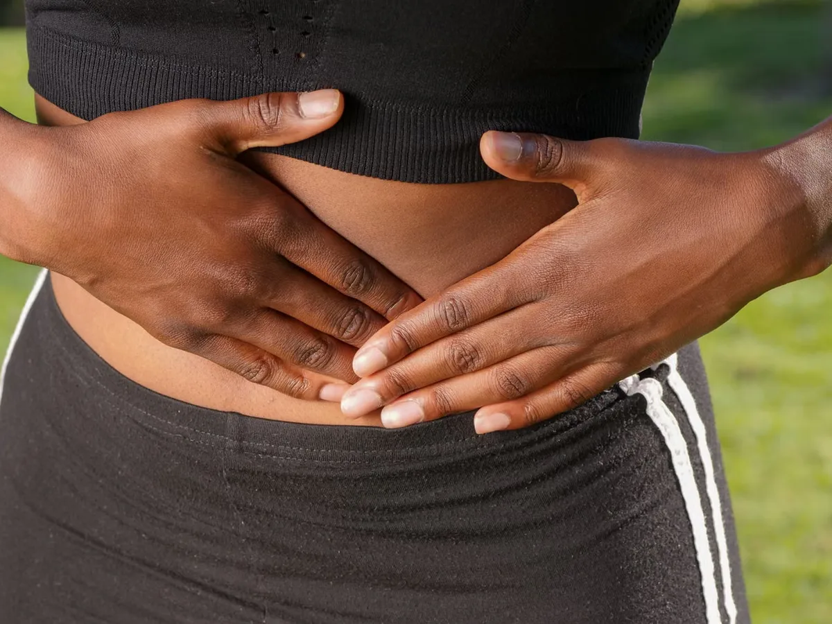Close-up of a woman resting both hands flat on her abdomen, holding her stomach during a bout of pain.