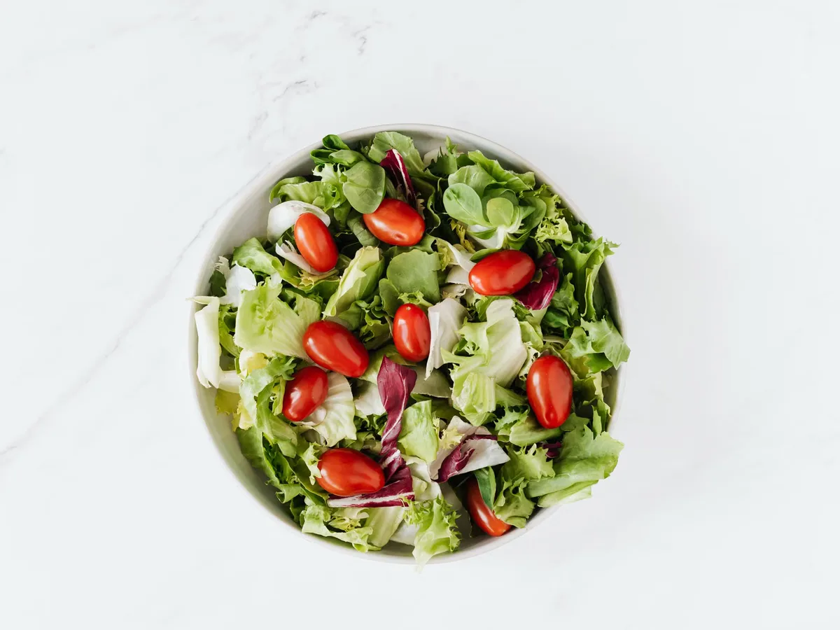 An overhead bowl of fresh green salad with grape tomatoes on a wooden table, the kind of vegetable-heavy meal that feeds good gut bacteria.
